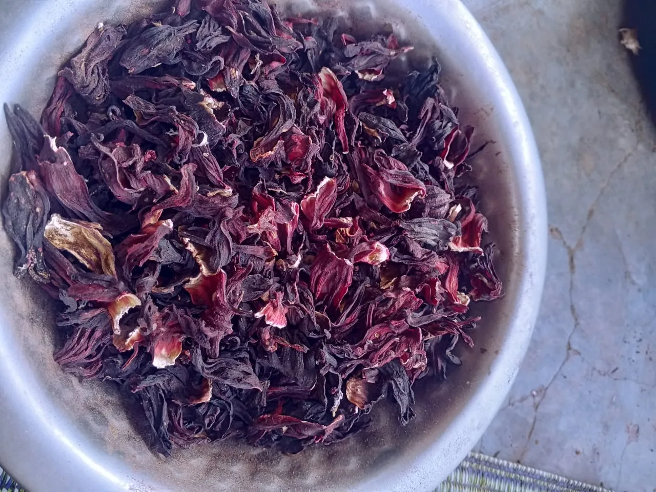 Des calices de bissap séchés, de couleur rouge foncé, dans un récipient.